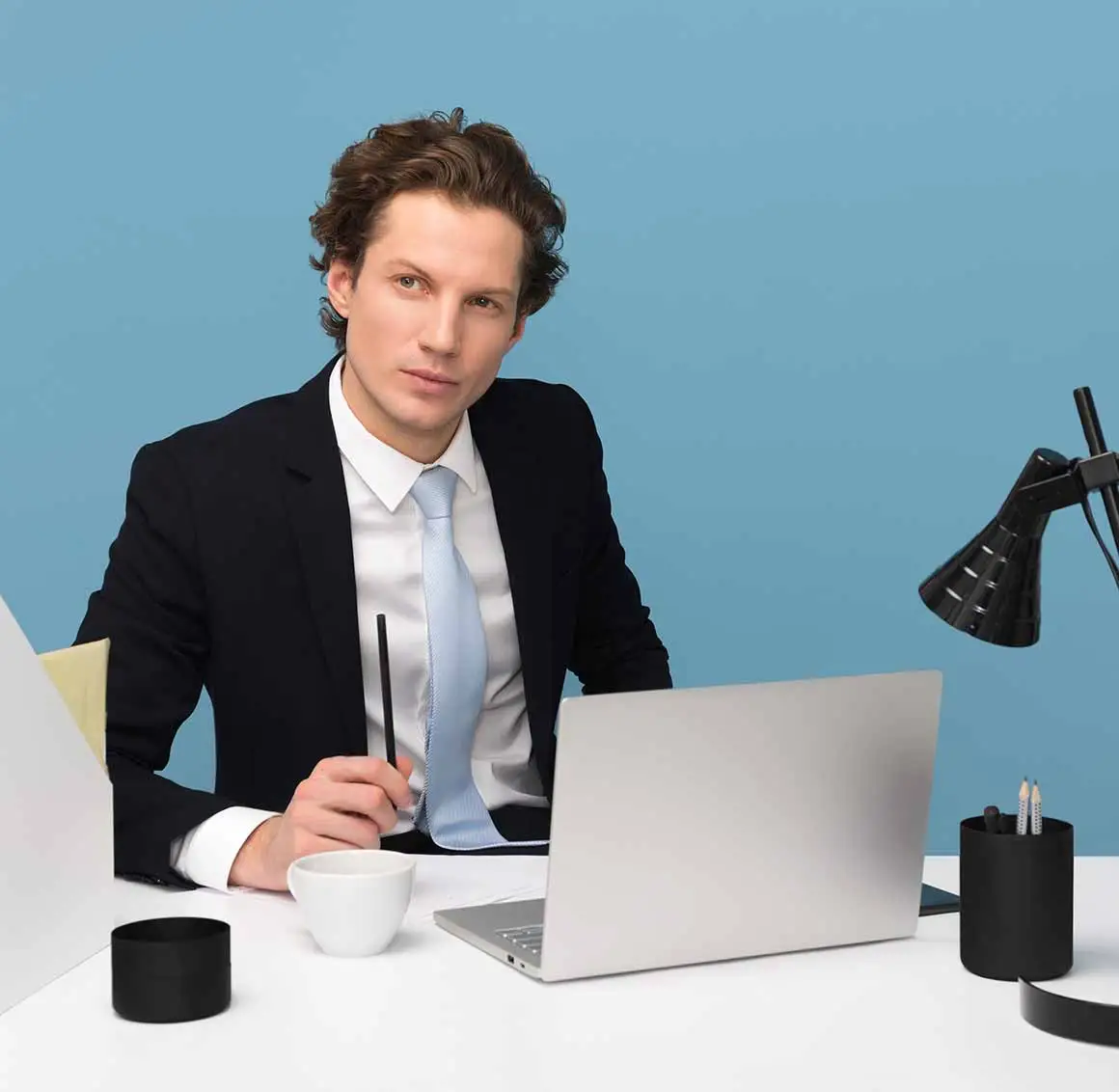 Tax consultant in a suit holding a pen, sitting in front of an open laptop, thinking about tax strategies and financial planning.